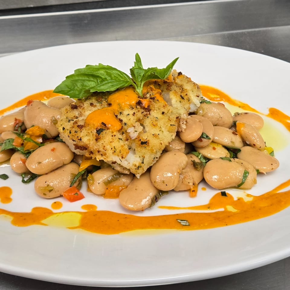 Crispy fish fillet with orange sauce, basil, and white beans on a white plate.