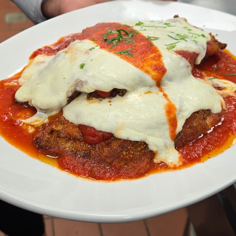 Chicken parmesan with melted mozzarella cheese, marinara sauce, and fresh herbs on a white plate.