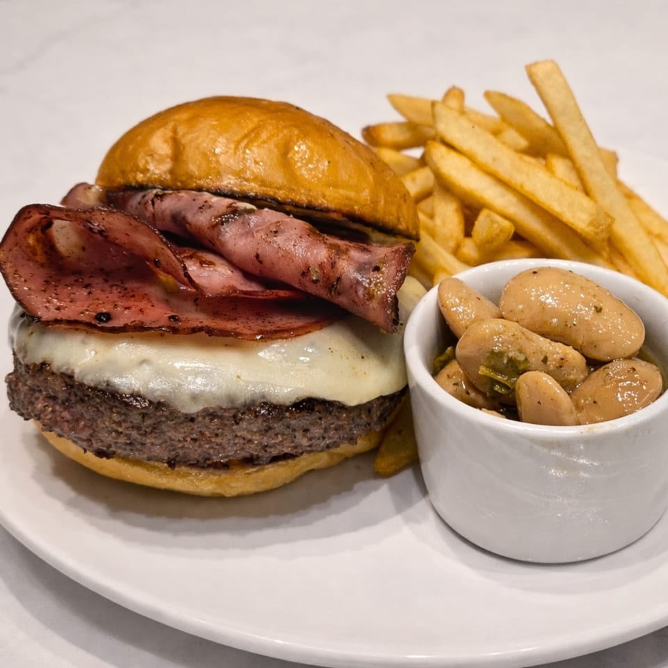 Cibo's burger with melted cheese, pastrami, fries, and a side of beans on a white plate.