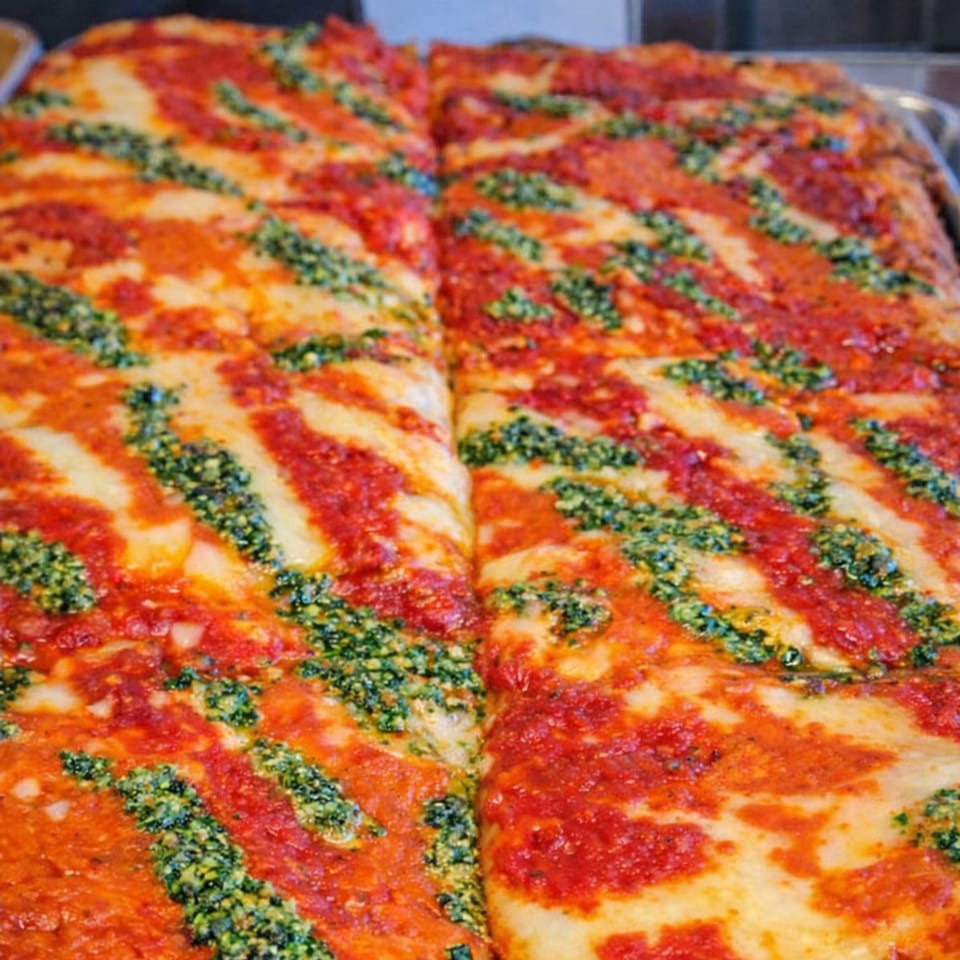Close-up of Cibo's rectangular pizza with red sauce and green pesto stripes, cut into two large halves.