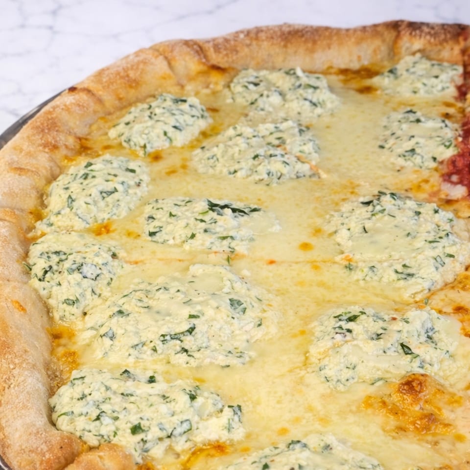 Close-up of a Cibo pizza with a thick crust, melted cheese, and dollops of ricotta.