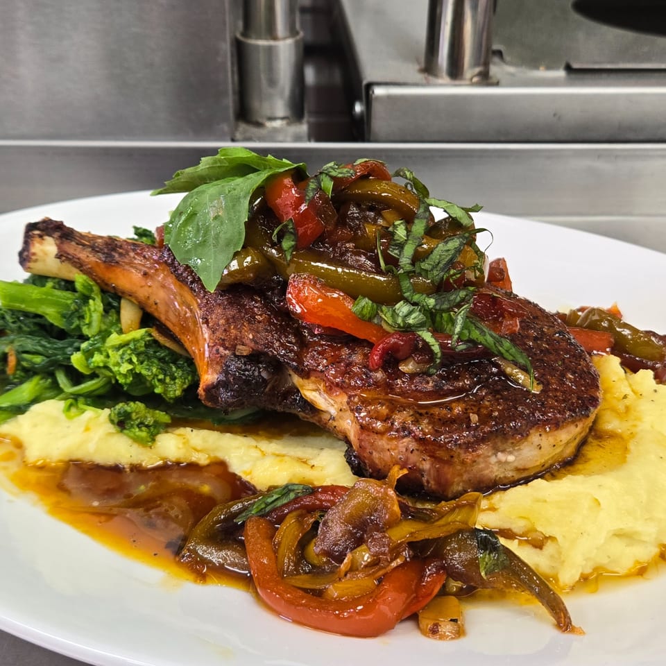 A Cibo pork chop with roasted peppers, broccolini, mashed potatoes, and a rich sauce.