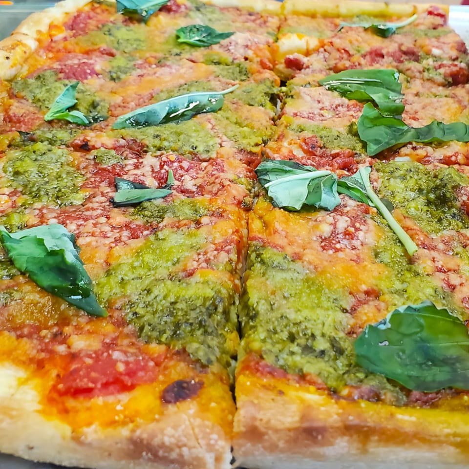 Cibo's pesto and tomato pizza, topped with fresh basil leaves, sliced and ready to serve.
