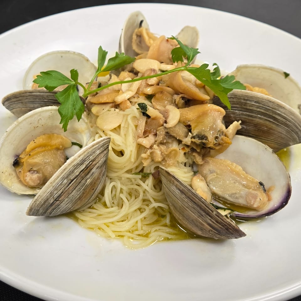 Clams and pasta with garlic and parsley on a white plate.