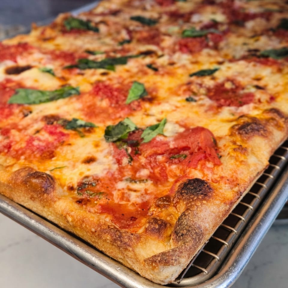 Close-up of a rectangular Cibo pizza with tomato sauce, melted cheese, and fresh basil.