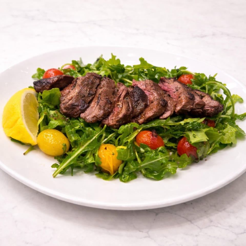 Grilled steak slices over a bed of arugula with cherry tomatoes and a lemon wedge.