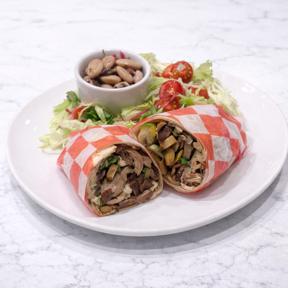 Two mushroom wraps with a side salad and a small bowl of beans on a white plate.